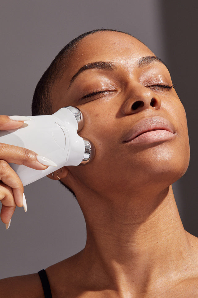 a photograph of a happy NuFACE customer using the TRINITY+ device on her jawline