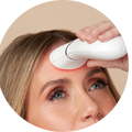 a photograph of a woman using the red light therapy attachment from the TRINITY+ device by NuFACE on her forehead