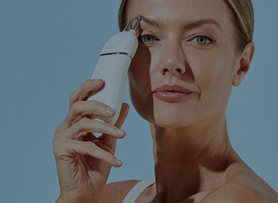a photo of a happy NuFACE woman using the TRINITY+ device with Eye Attachment on her eyebrows