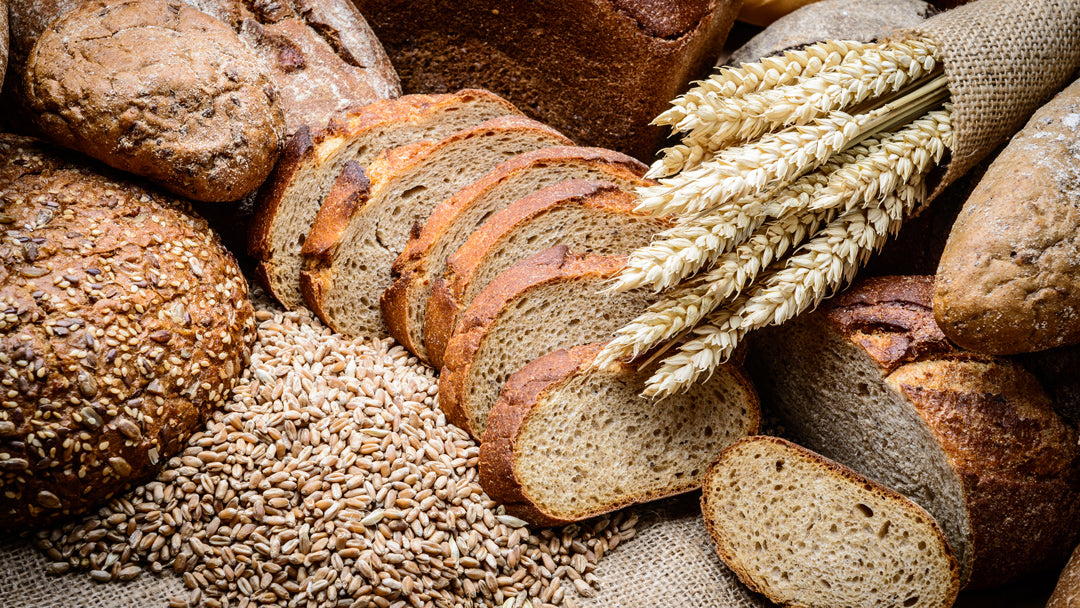 a photograph of multiple types of bread, sliced and whole, and grains, ground and whole