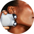 a photograph of a woman using the grey MINI+ device by NuFACE on her jawline